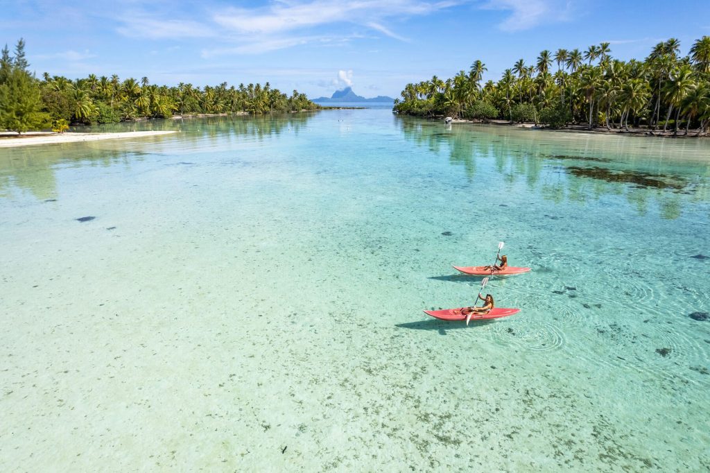 | Blue Tahiti Travel Couple Kayaking in the Turquoise Lagoon at Le Taha'a by Pearl Resorts, Surrounded by Stunning Views and Serene Tropical Beauty in French Polynesia.