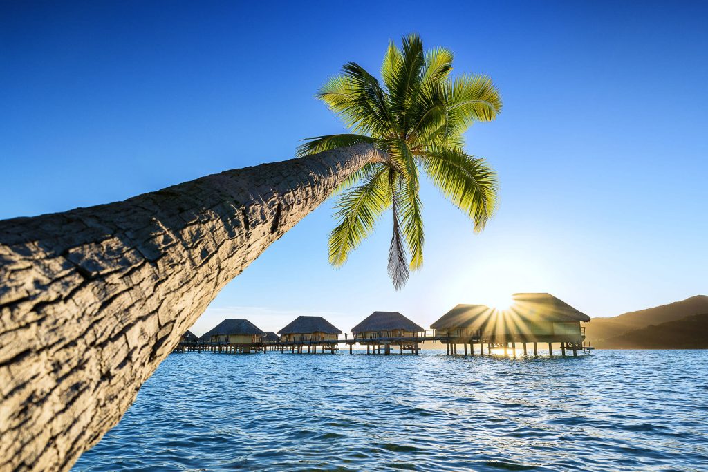 | Blue Tahiti Travel Sunset over the Overwater Bungalow Pontoon at Le Taha'a by Pearl Resorts, Casting a Golden Glow Across the Tranquil Lagoon in French Polynesia.