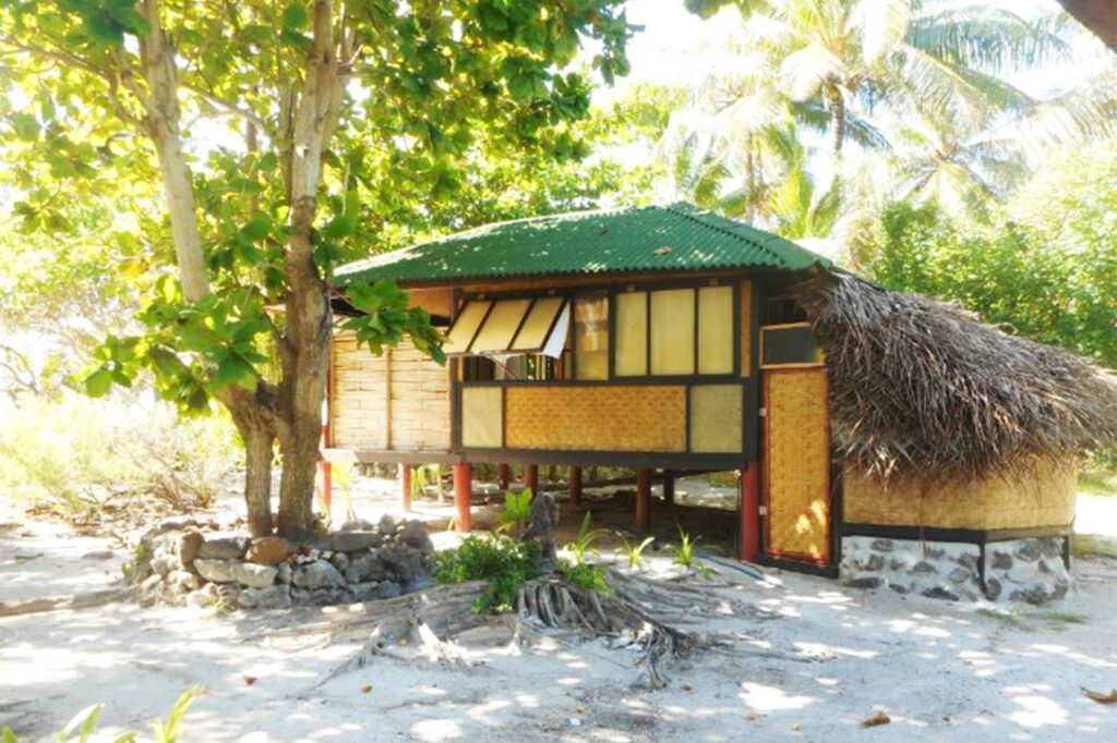 | Blue Tahiti Travel Exterior View of Traditional Bungalows at Pension Le Kuriri, Maupiti, Handcrafted from Natural Materials and Nestled in Lush Island Surroundings.
